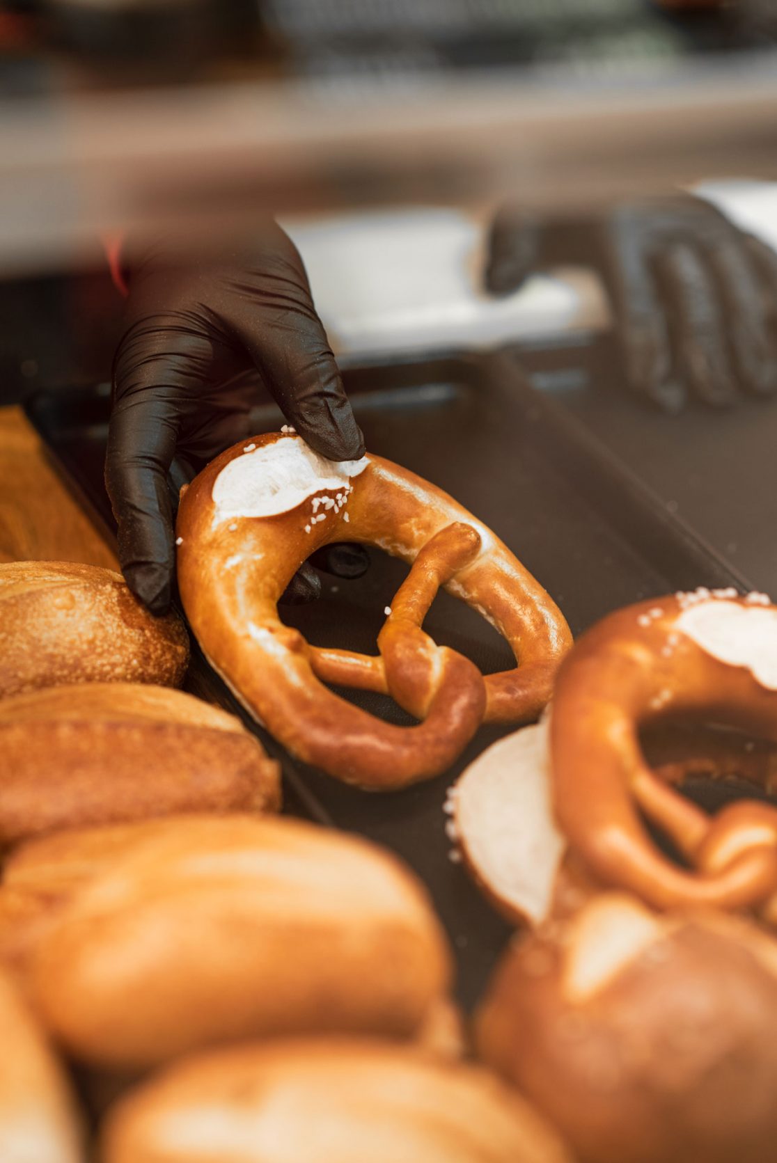 Hand mit schwarzem Handschuh entnimmt Brezel von der Auslage