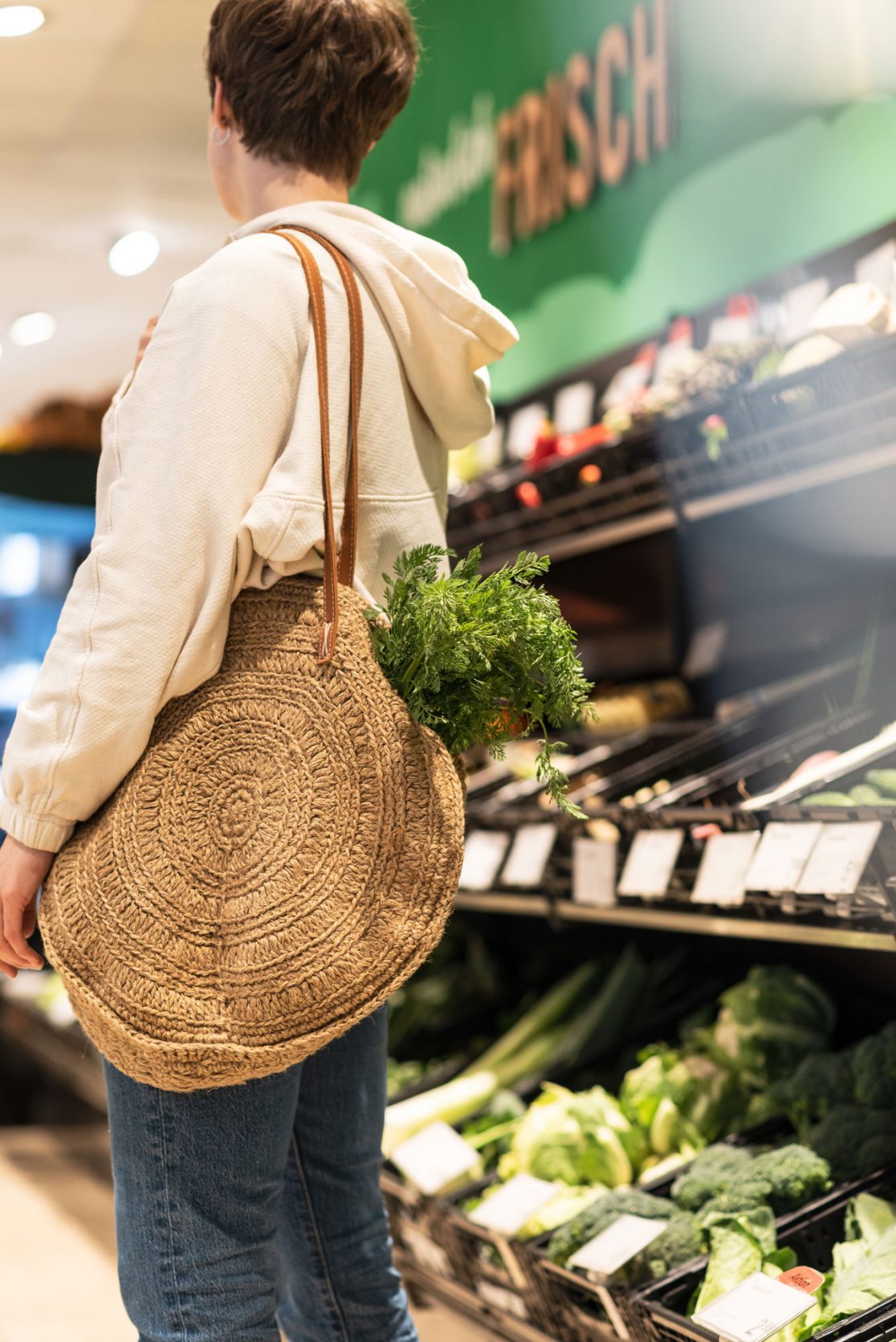 Person mit Basttasche vor dem Gemüseregal