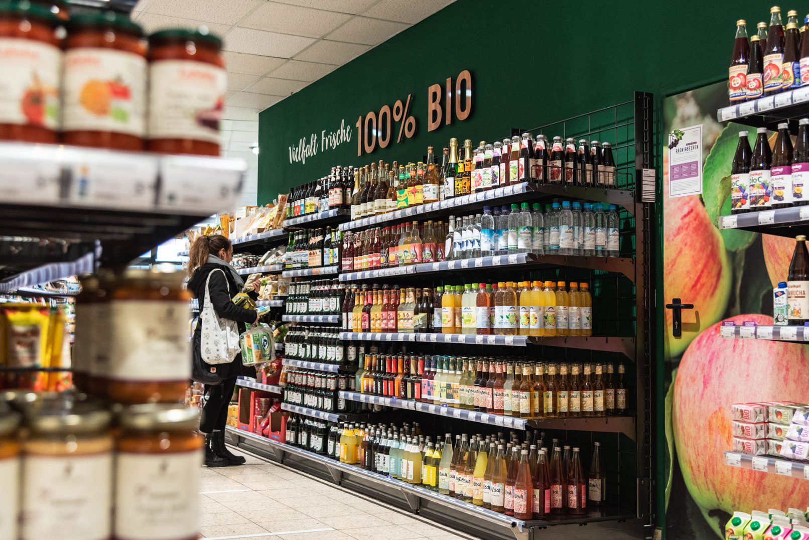 Person steht vor einem Regal mit Getränken mit Tasche und Einkäufen